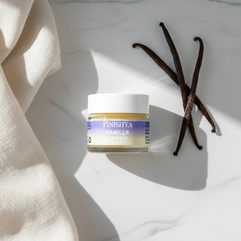 Finishya Vanilla Lip Balm jar styled with real vanilla beans on a marble surface to emphasise the gourmand fragrance.