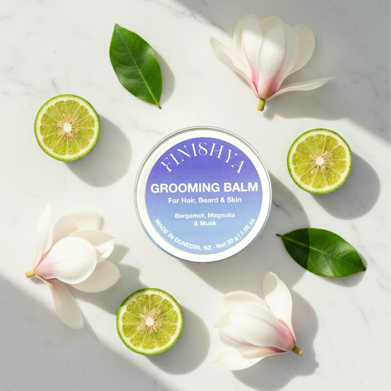 Flatlay of Finishya Grooming Balm surrounded by fresh bergamot slices and white magnolia flowers to represent the fragrance notes.