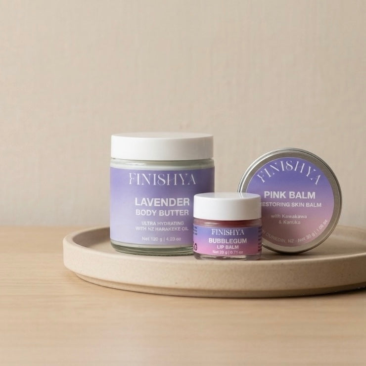 Cruelty-free and vegan skincare products for sensitive skin by Finishya. Shown: Lavender Body Butter, Pink Balm skin restorer, and Bubblegum Lip Balm on a minimalist ceramic tray.