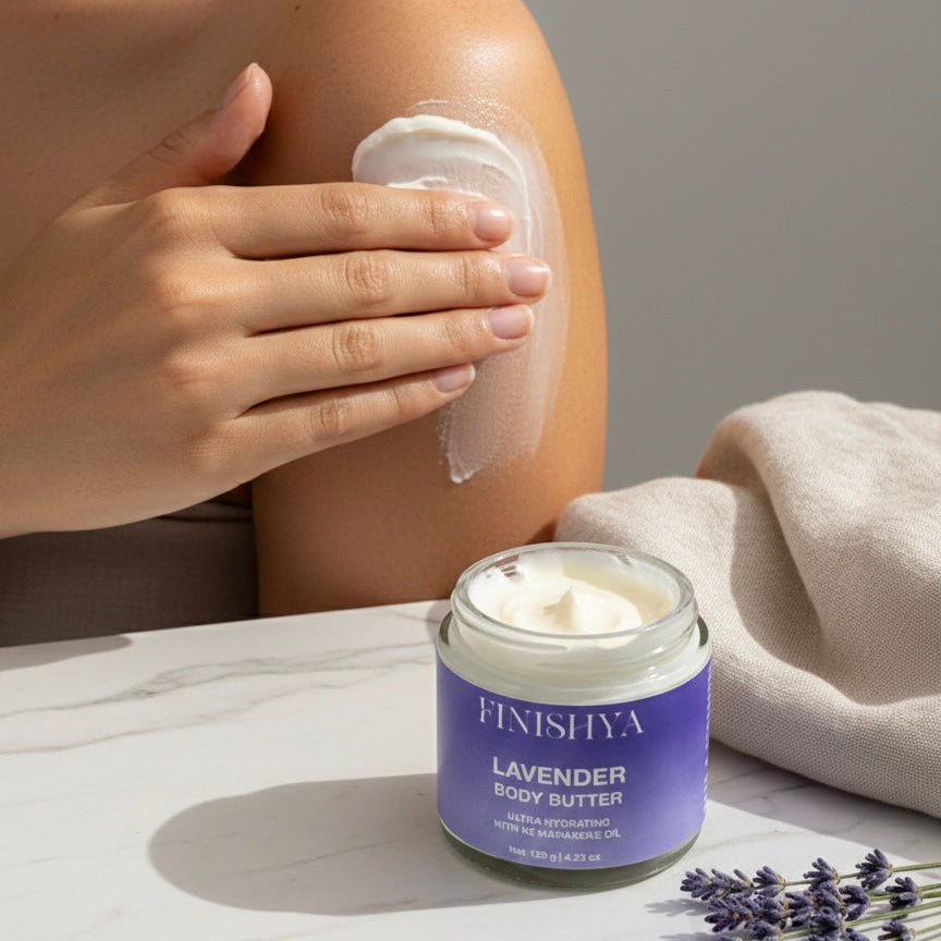 A person applying Finishya Lavender Body Butter to their shoulder. The white cream is spread across the skin, highlighting its smooth application. A jar of the vegan body butter and dried lavender sprigs are in the foreground.