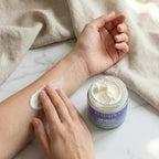 A person applying Finishya Jasmine Body Butter to their inner arm. The hydrating cream is being massaged into the skin next to an open glass jar, emphasising its smooth, non-greasy texture.