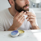 A man applying Finishya Grooming Balm to his beard for softening and styling in a modern bathroom setting.