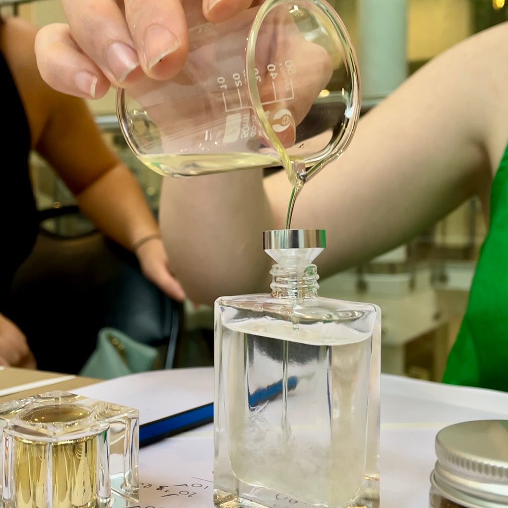 Close-up of a participant carefully pouring a bespoke, cruelty-free fragrance into a clear glass perfume bottle using a funnel.