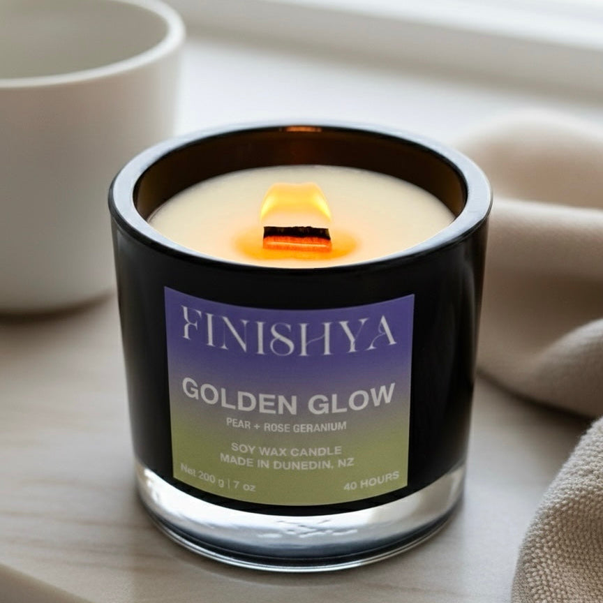Close up of a lit Finishya Golden Glow candle with a steady flame on a wooden wick, styled in a modern, minimal interior setting.
