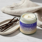 An open jar of thick, creamy white vanilla body butter next to whole vanilla beans on a marble surface.