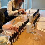 A long table arranged with amber glass dropper bottles and blending supplies for a Finishya perfume workshop.