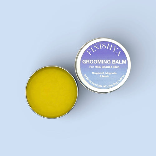 An open 30g tin of Finishya Grooming Balm showing the smooth yellow texture beside the purple and blue label lid.