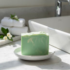 Finishya Jasmine hand and body soap on a white dish in a sunlit marble bathroom, styled with fresh white jasmine flowers.