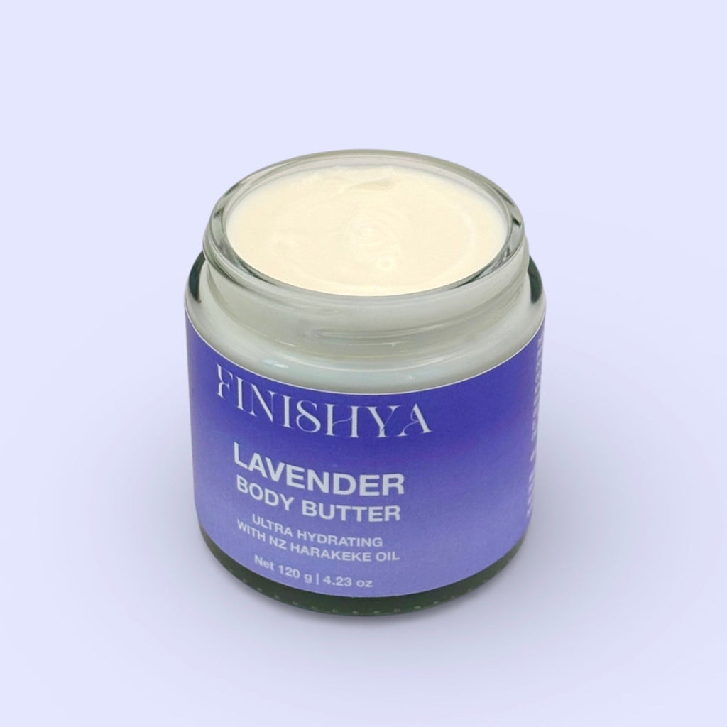 Top-down angled view of an open jar of Finishya Lavender Body Butter. The 120g glass jar shows the cream texture inside against a soft lilac background.