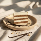 A top-down view of a Vanilla soap bar on a ceramic plate, styled with whole vanilla beans on a textured linen cloth.