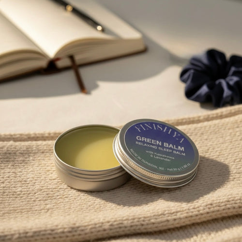 Finishya Green Balm open on a bedside table next to a notebook, highlighting its use in a relaxing nightly sleep ritual.