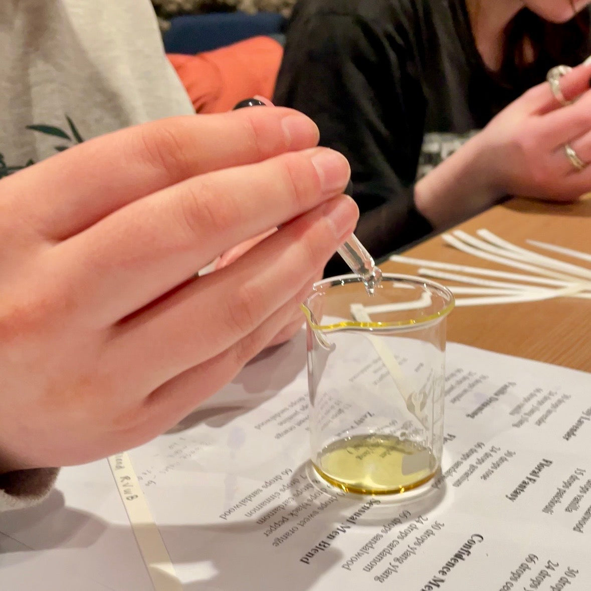 Hands using a glass dropper to add essential oils into a beaker during a Finishya fragrance workshop.