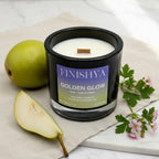 A black glass soy candle with a wooden wick sitting on a marble surface next to a fresh sliced pear and pink geranium flowers.