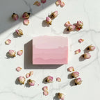 Overhead view of a pink gradient Rose soap bar on marble, surrounded by dried rose buds and delicate pink petals.