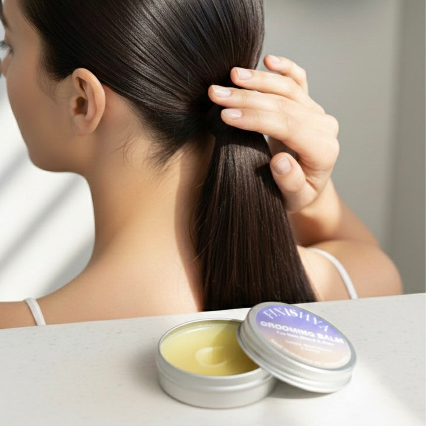 A woman styling a sleek, smooth ponytail with Finishya Grooming Balm to settle baby hairs.