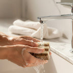 Person lathering a textured Vanilla soap bar under running water in a bright bathroom, showcasing its creamy foam for sensitive skin.