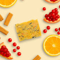 Flat lay of NES Wild Orchard Artisan Soap with orange, pomegranate, red currant, and sandalwood – vibrant natural ingredients surround the handcrafted soap.